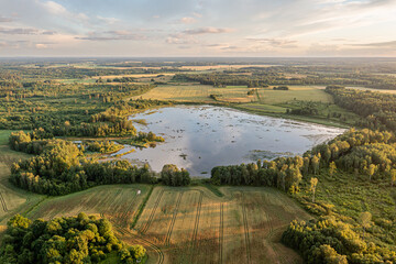 Vast landscape with tranquil lake surrounded by lush greenery and farmland at sunset