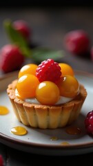 A delicious tart topped with vibrant yellow spheres and a fresh raspberry, surrounded by scattered red berries on a dark background