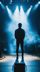 Silhouetted figure on stage, spotlights, smoke.
