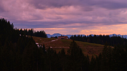 Sunset over tranquil hills with a cabin nestled among the trees and mountains in the background