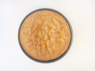 Top view of a freshly baked sponge cake in a round baking pan, showing the golden-brown texture.