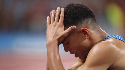 Fototapeta premium Young male athlete in distress, holding his head in frustration after a race.