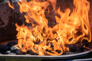 Charcoal burning in a grill with visible orange flames and black coals, high heat for barbecue cooking.
