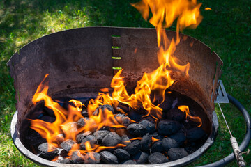 Charcoal burning in a grill with visible orange flames and black coals, high heat for barbecue...
