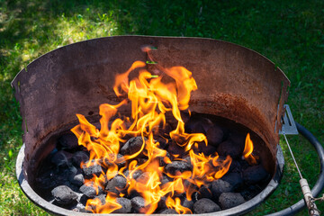Charcoal burning in a grill with visible orange flames and black coals, high heat for barbecue...