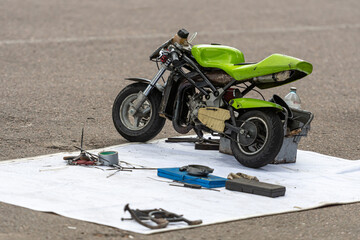 Small green motorcycle on a repair mat surrounded by tools and equipment