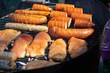 Close-up of seasoned sausages and marinated chicken grilling over hot coals on a barbecue.