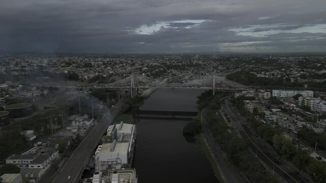 Drone flies north along the Ozama River and flies over the Juan Pablo Duarte Bridge on cloudy day in Santo Domingo, Dominican Republic