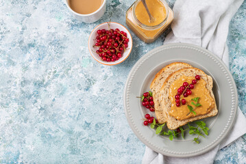 Whole grain sandwich with peanut butter, mint and red currant top view. Breakfast on blue background with copy space