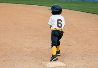 A six year old baseball player boy on first base ready to run.