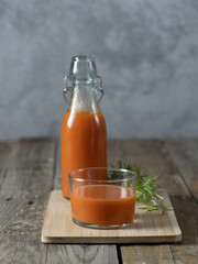 Vertical photo of a glass of gazpacho and a bottle in the background on a tray isolated on a wooden background