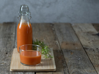 A horizontal photo of a glass of gazpacho and a bottle in the background on a tray, isolated on a wooden background. Copy space