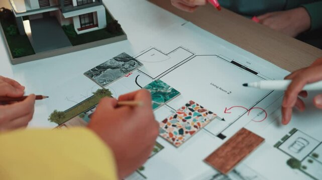 Diverse hands examine vibrant floor plans and material samples during a brainstorming session, showcasing collaboration in innovative architectural design and planning. SACTR