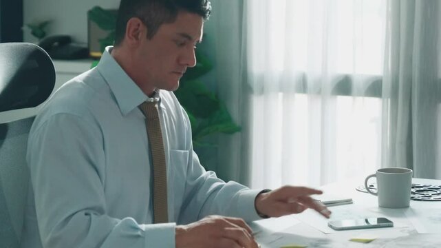 Professional engineer looking at phone while working on tablet with green screen at meeting table with turbine engine or jet engine sketch design and various metal gear scatter around. Alimentation.