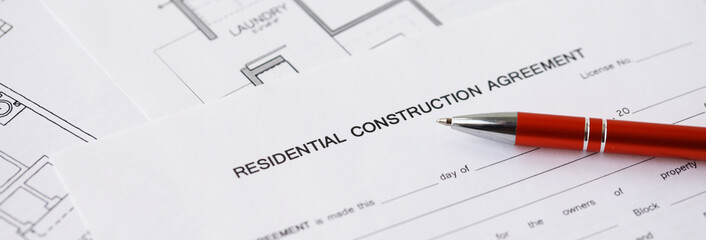 Pen on residential construction agreement and planning blueprints of residential building project...