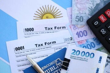 Argentine pesos money bills in big amount lies on table with pen, calculator, passport and tax forms