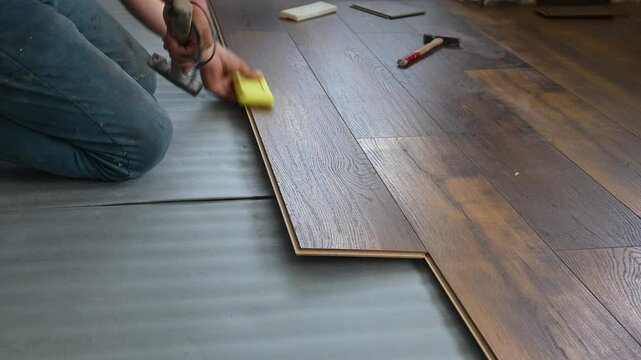 The master is laying laminate flooring on the floor of the house.