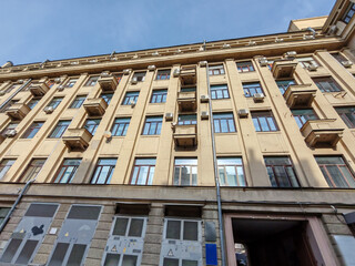 Fototapeta premium An upward view of a beige residential building with numerous windows, small balconies, and air conditioning units. The photo highlights urban density and the geometric symmetry of functional