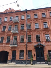 Fototapeta premium A tall red brick building featuring elaborate decorative elements, black iron balconies, and arched ground-floor entrances. The image reflects the grandeur and craftsmanship of vintage city