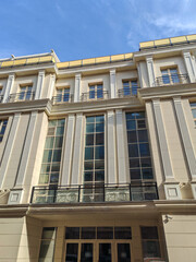 Elegant cream-colored building featuring symmetrical columns and intricate balcony railings. Its grandeur reflects themes of luxury, stability, and hidden urban sophistication.
