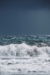 Dramatic ocean waves crashing against a rocky shore under a moody blue sky