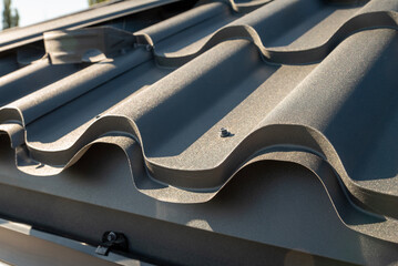 Metal waves of shingles shimmer under the golden sunlight and snow retainer