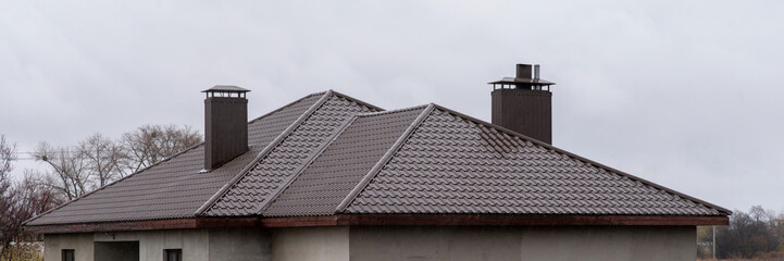 Brown metal roof with wet surface and chimneys