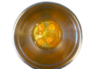 Top view of cracked eggs in a stainless steel mixing bowl, showing raw eggs ready for baking or...