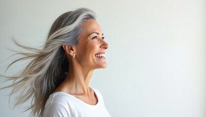 Portrait mature woman with silvery grey hair smiling against white backdrop. Windswept hair, radiant smile, capturing beauty age. Side view of a happy lady enjoying her life.