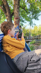 Student resting during summer holidays, boy lying in hammock and looking at smartphone, online learning, outdoor recreation during summer holidays