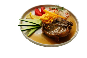 Juicy fried meat in sauce on a plate with French fries, salad, and slices of lemon, tomato, and cucumber — presented on a white background.
