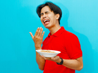 portrait of Asian man in a red polo shirt holding a plate of fried noodles showing a funny facial...
