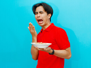 portrait of Asian man in a red polo shirt holding a plate of fried noodles showing a funny facial...