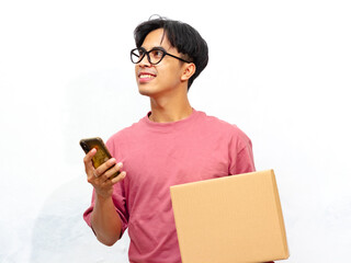 Portrait of a young Asian man in a pink t-shirt, smiling and holding a mobile phone and a package...