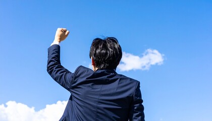 青空を見上げてガッツポーズする若いビジネスマン