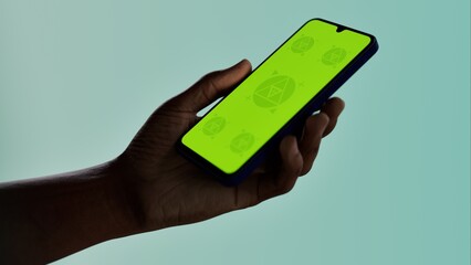 Black African-American young male using smartphone with a blank green screen. Mobile app video mockup. Vertical phone orientation