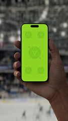 GREEN SCREEN CHROMA KEY A hand holding a phone with a green screen at a hockey game in an indoor stadium, ideal for showcasing live sports or betting apps