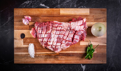 Suadero de res crudo.  Trozo de carne de ternera sobre tabla de madera con  verduras, hierbas y sal sobre fondo oscuro. Vista superior y espacio de copia.