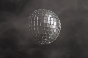 A glittering disco ball against a dramatic black backdrop with smoke, evoking the atmosphere of...
