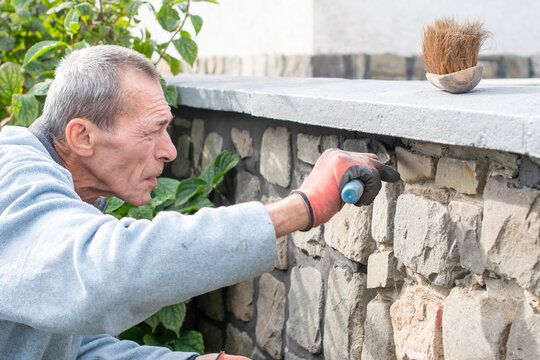 A builder carefully applies cement between the stones of a wall with a narrow trowel, restoring the appearance of a historic building using professional methods and tools