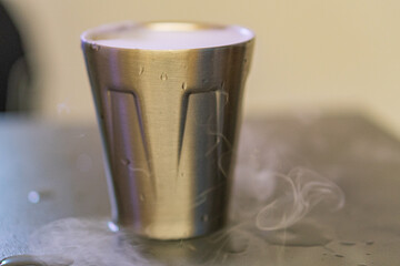 A close-up image of a hot, frothy beverage in a gleaming silver cup, evoking luxury and comfort, suitable for advertising gourmet coffee shops or promoting hot beverages