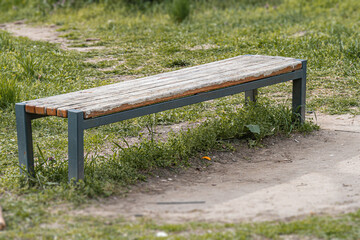 An unoccupied, weathered wooden bench with metal legs in a natural outdoor setting The ground is...