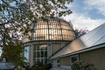 Fototapeta premium Modern architectural structure with a central round glass pavilion, green foliage surrounding, green roof sections, soft lighting, and still serene mood