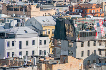 Fototapeta premium Cityscape with various buildings, overhanging canopy structure under construction, scaffolding and material coverings, urban environment, muted earthy tones, overcast sky, rooftops, pitched roofs, mu