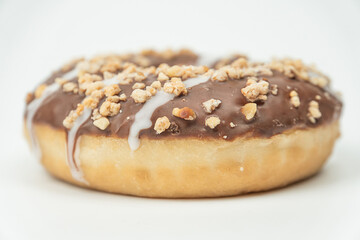 Close-up of a chocolate-glazed doughnut with chopped nuts and swirled lighter icing, placed on a white surface with subtle gradient lighting