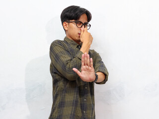 Young handsome Asian man covering his nose with his hand while showing a stop gesture with his...