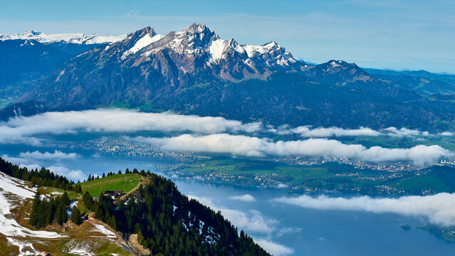 Mountains and clouds above lake with small village nestled in green valley on a clear spring day