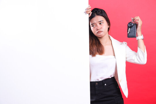 A woman with light brown hair and wearing a white jacket is holding a car key and standing behind a white blank board, isolated on a red background
