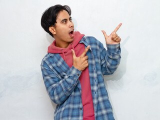 Excited young Asian man posing and pointing to the side to showcase an advertisement.