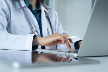 Close up, doctor working on laptop computer with digital tablet on office table. Female doctor searching the patient health information, using laptop and tablet. healthcare and medicine concept